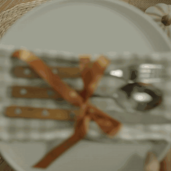 Décoration de table d’automne dans des tons marron et camel, avec des citrouilles lumineuses en verre doré, un set de table vert clair à pois, une bougie votive et des verres striés.